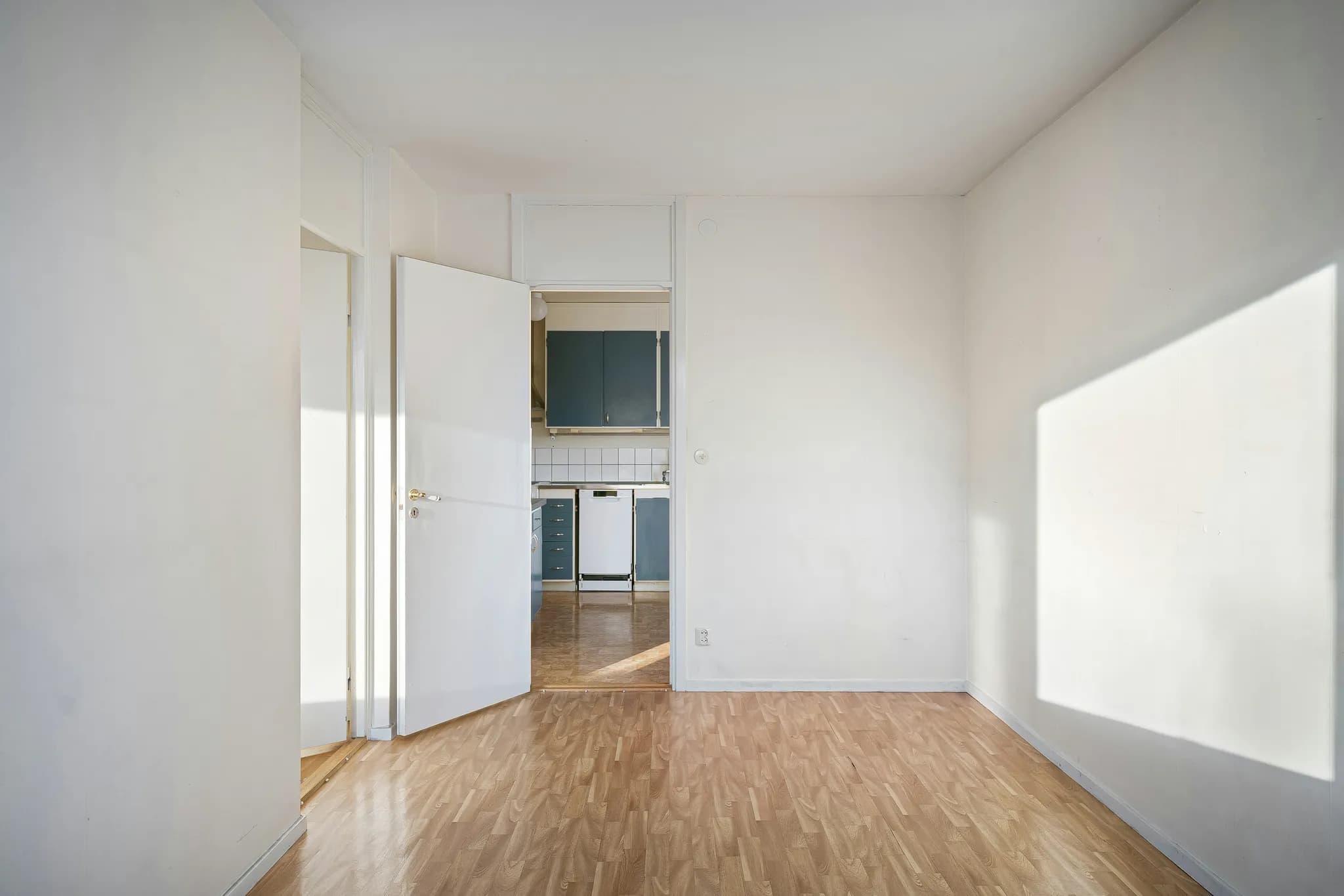 An entrance hall with white walls, a wooden floor and an open door to the kitchen