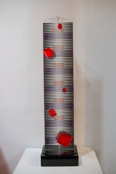 A tall silver plexiglass tower by Hugo Diaz with red and yellow cubes fixed to its face