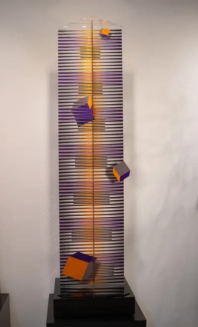 A tall plexiglass tower by Hugo Diaz lit from within, with coloured cubes fixed to its face