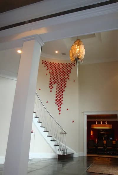 A cascade of small red steel elements by Carolina Sardi falling down a tall stairwell wall