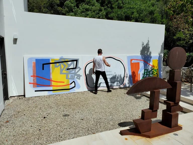 A painting by Scott Ashley hung on an outdoor wall, with rusted steel sculptures standing in front of it