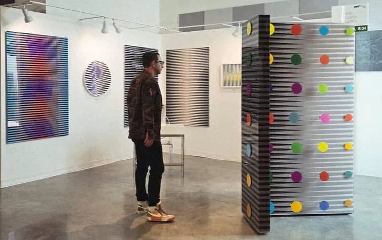 Works by Hugo Diaz in a fair booth, with a visitor standing among them