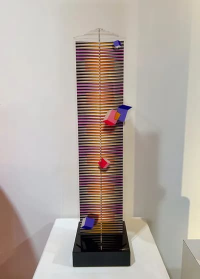 A tall plexiglass tower by Hugo Diaz striped in orange and violet, with coloured cubes fixed to its face