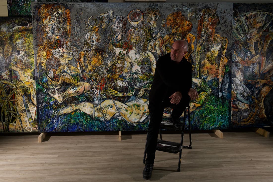 Fredy Villamil seated in front of his painting Muse