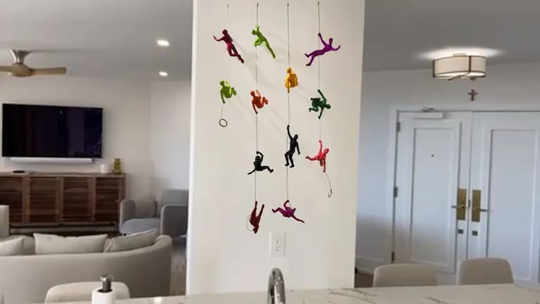 Small coloured climbing figures by Ancizar Marin arranged up a wall panel in a room