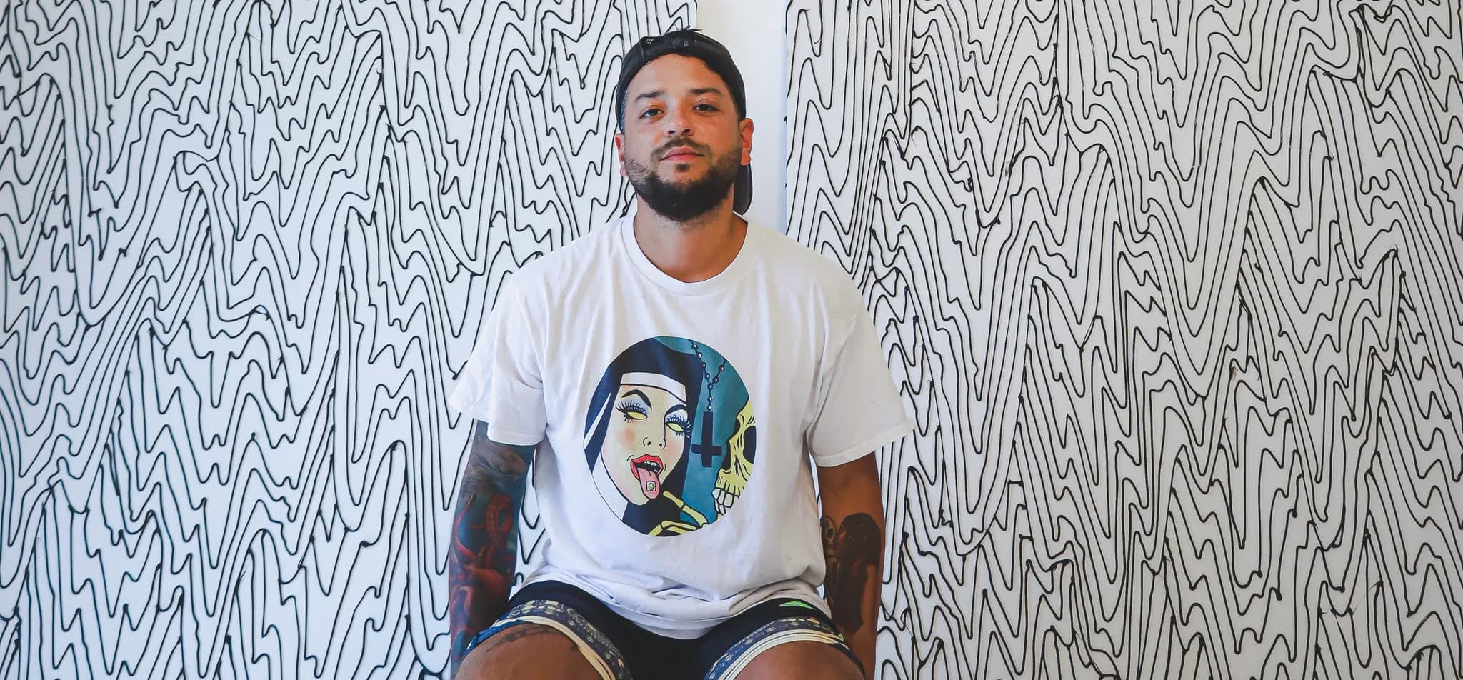 Enrique Machado seated in front of a wall covered in his black wave line drawing.