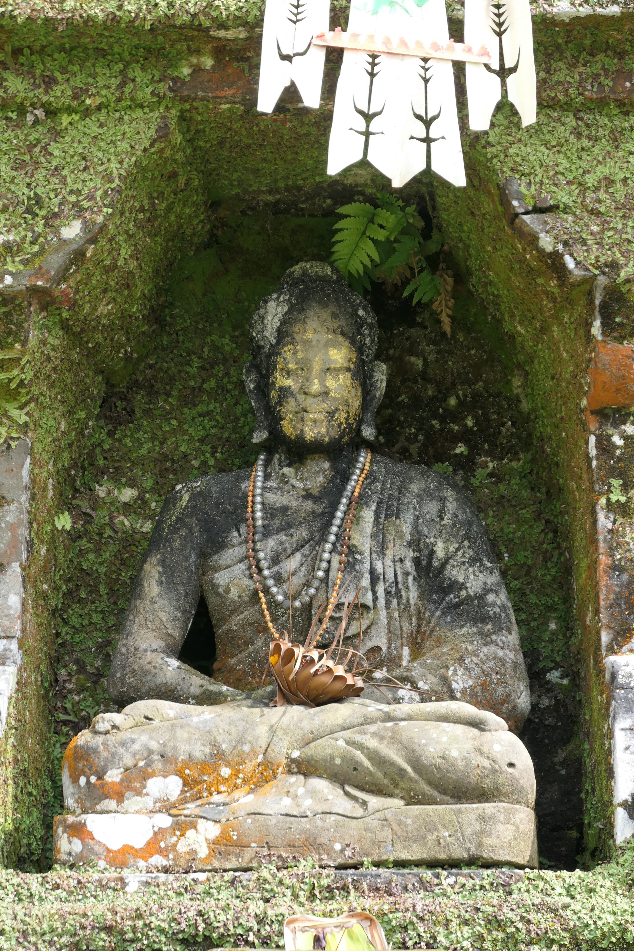 A seated stone Buddha in a mossy shrine at Pura Ulun Danu Beratan, Bali