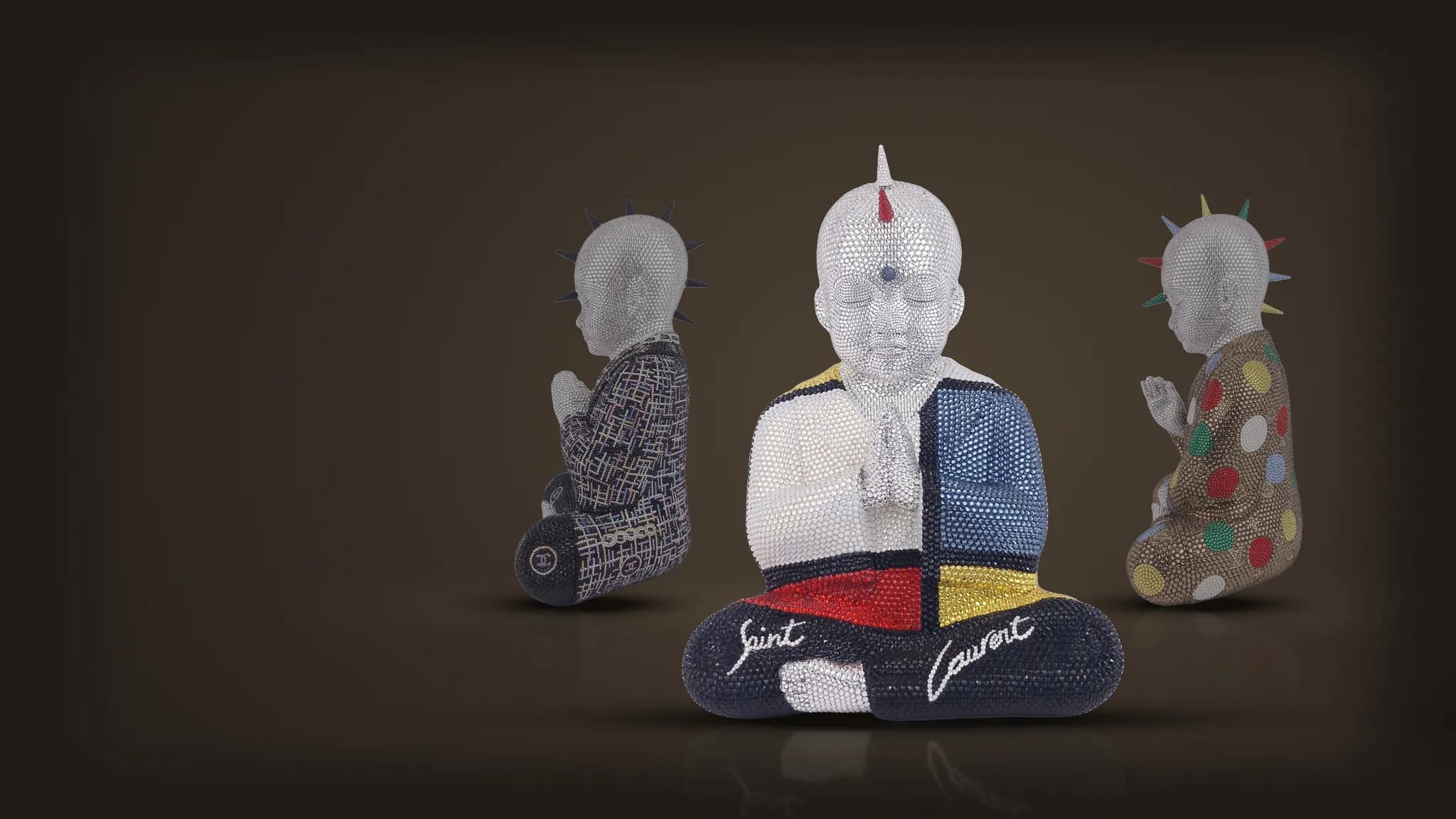 Three crystal Punk Buddhas by Metis Atash on a dark stage: Saint Laurent Mondrian in front, Mademoiselle Chanel and Kusama Vuitton in profile behind